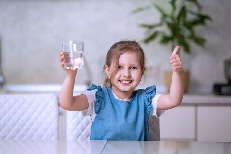 Niña sonriente mostrando un vaso de agua limpia en su cocina